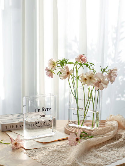 Clear acrylic vase shaped like an open book, holding fresh stems