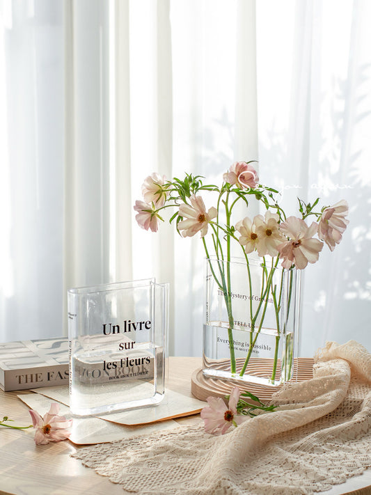 Clear acrylic vase shaped like an open book, holding fresh stems